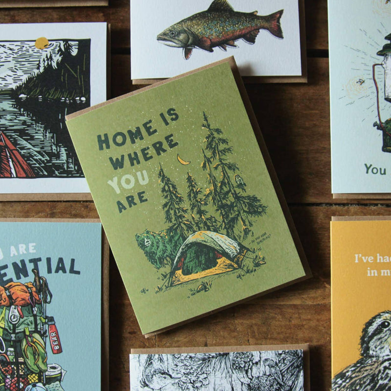 "Home is where you are" card depicts a tent in the woods with a bear and owl, highlighting joy in outdoor companionship.