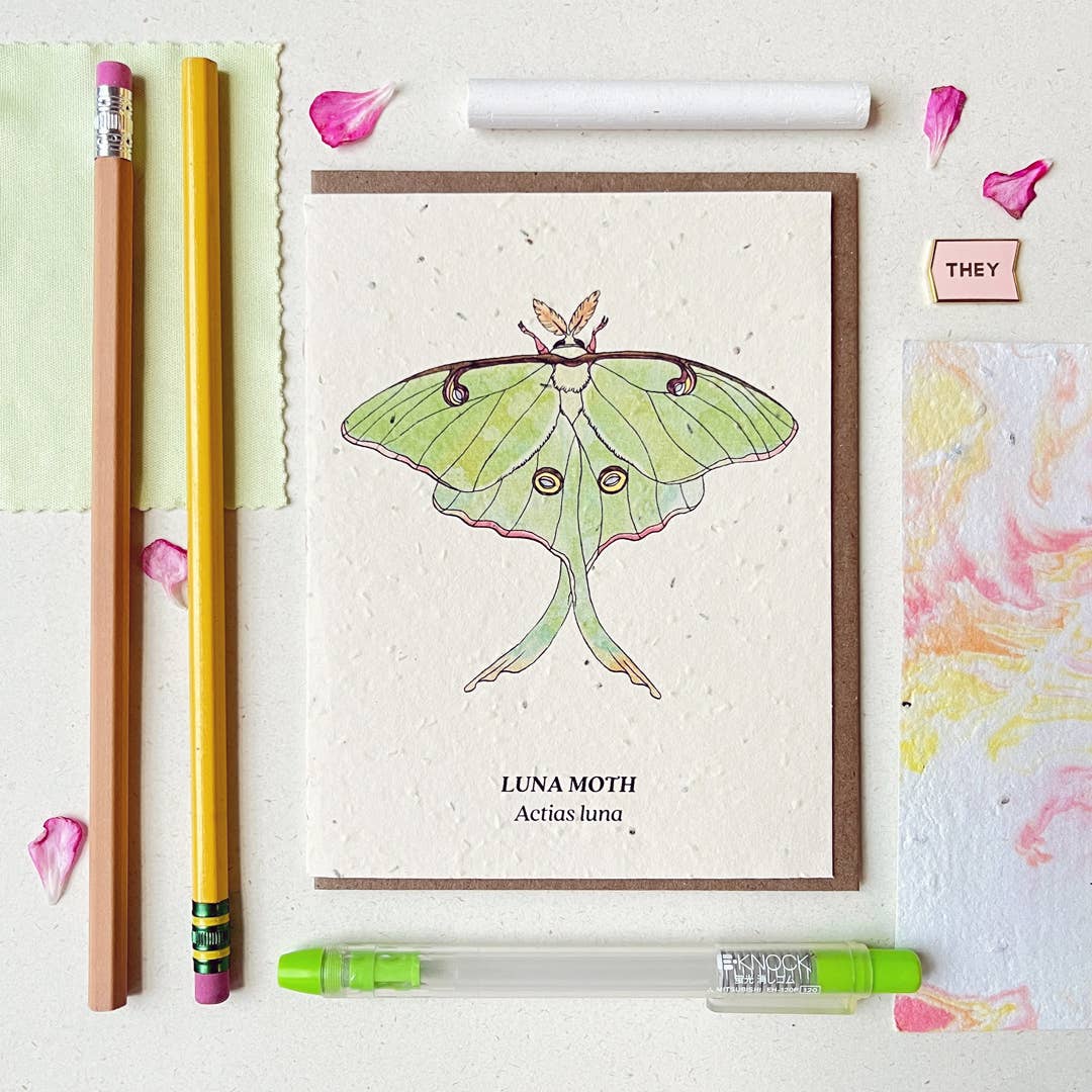a plantable card depicting a green luna moth surrounded by green office supplies