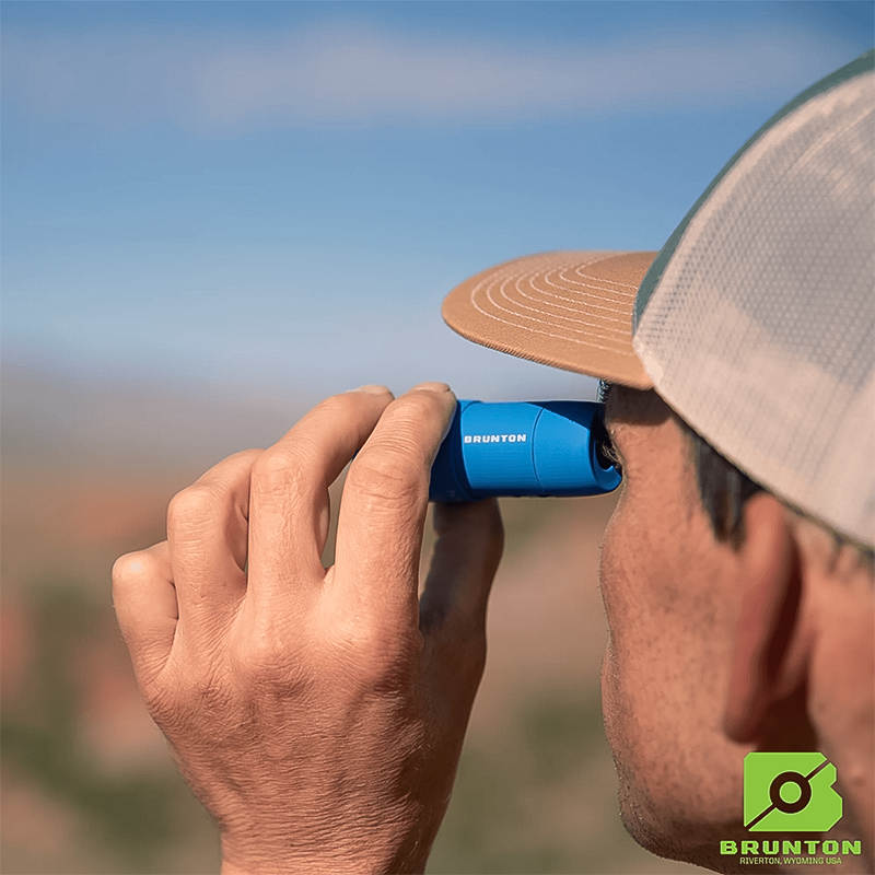 A man looks through a blue Brunton Echo Pocket Scope binocular.