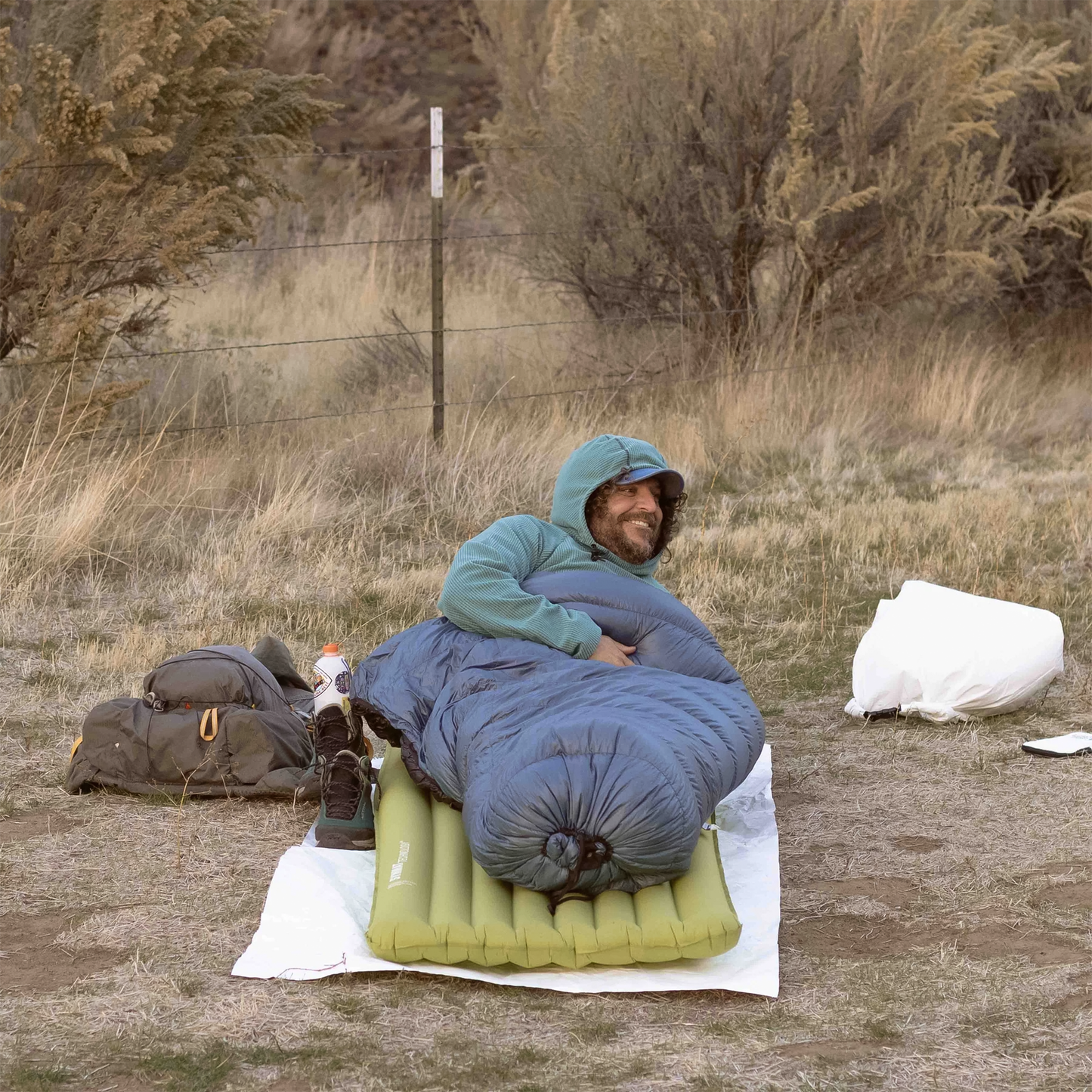 A man lies on a sleeping bag outdoors, showcasing the Cowboy Camping Claim Jumper groundsheet providing a clean, dry surface.