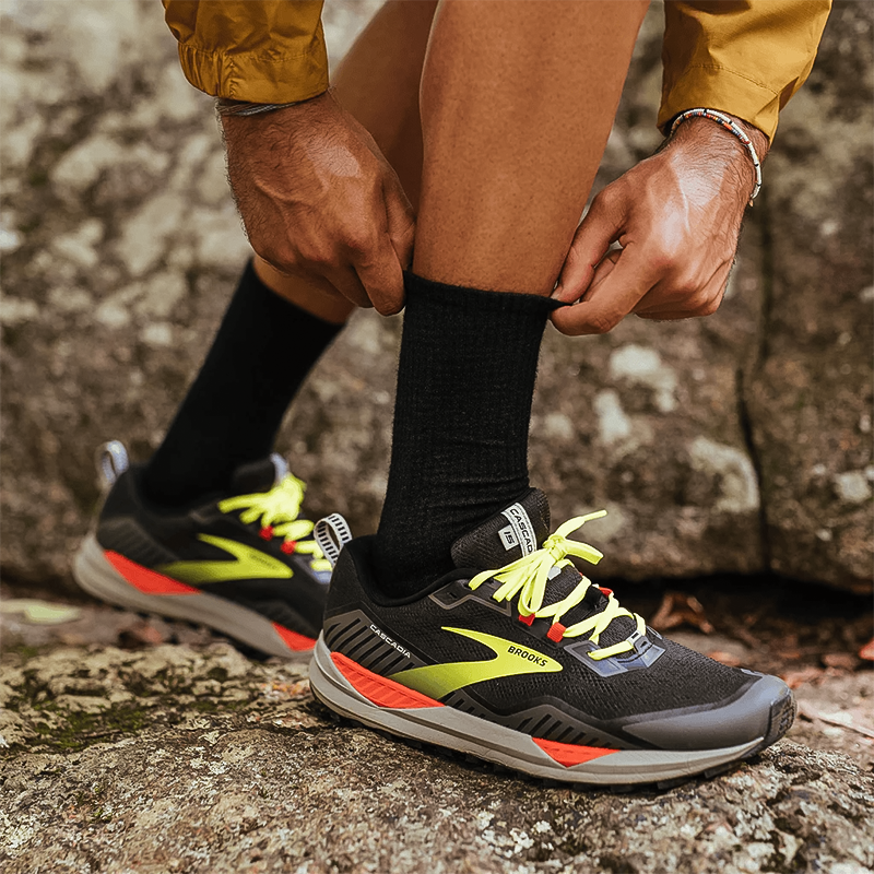 A man on a rock displays his running shoes and Feetures Merino 10 Ultra Light Mini Crew socks in Black.