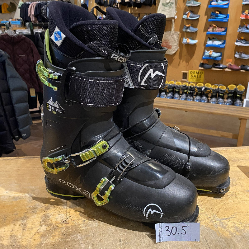 Pair of black ski boots with green accents on a wooden surface in a store setting.