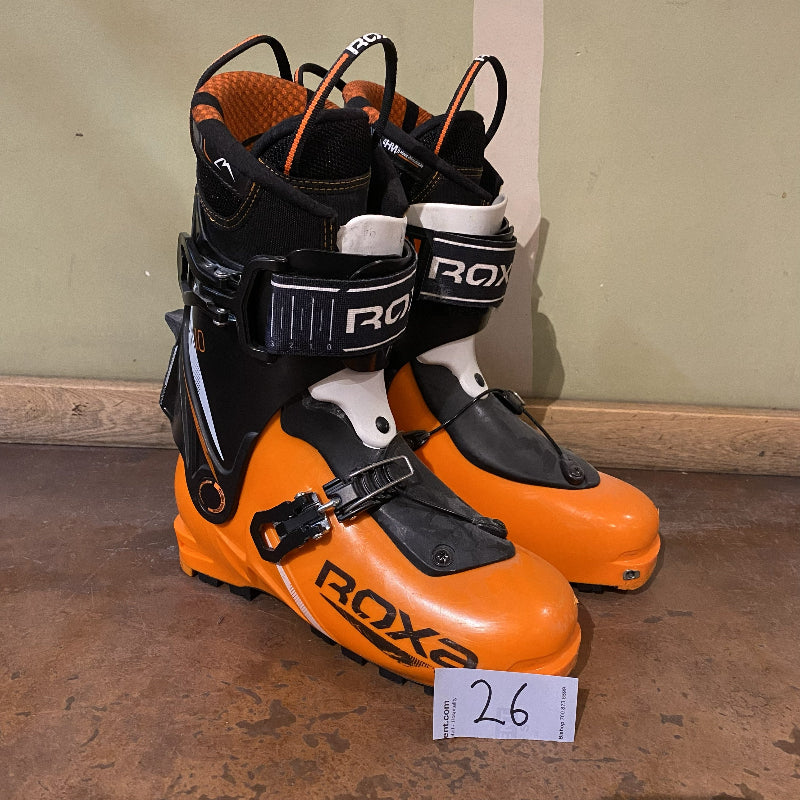 Pair of orange and black ski boots with 'ROXA' branding on a concrete floor.