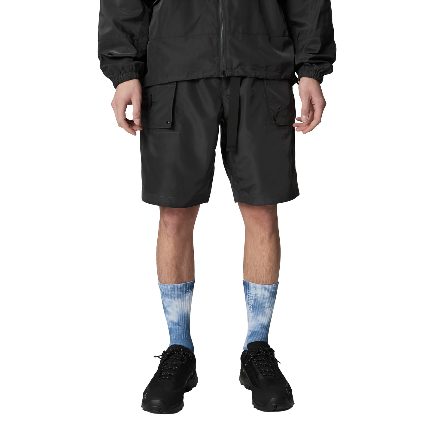 A man in a black jacket and shorts stands outdoors, showcasing Rúngne Nomad Socks designed for comfort and breathability.