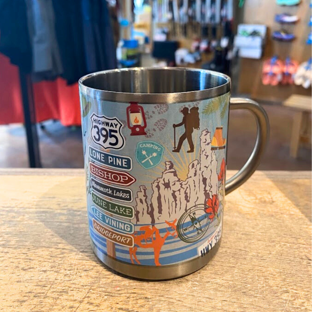 A stainless steel mug with colorful printed designs including text and images related to Highway 395 and camping.