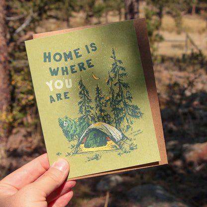 Card reads "Home is where you are," showing a tent in the woods with a bear and owl, celebrating outdoor connections.