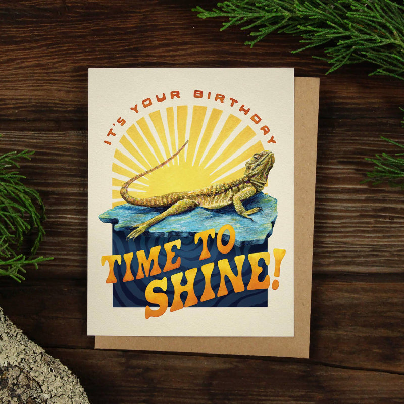 Birthday card featuring a cheerful lizard basking in sunlight, with the text "It's your birthday, time to shine!" on the front.