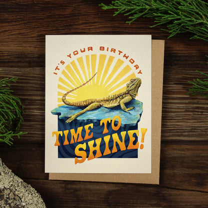 Birthday card featuring a cheerful lizard basking in sunlight, with the text "It's your birthday, time to shine!" on the front.