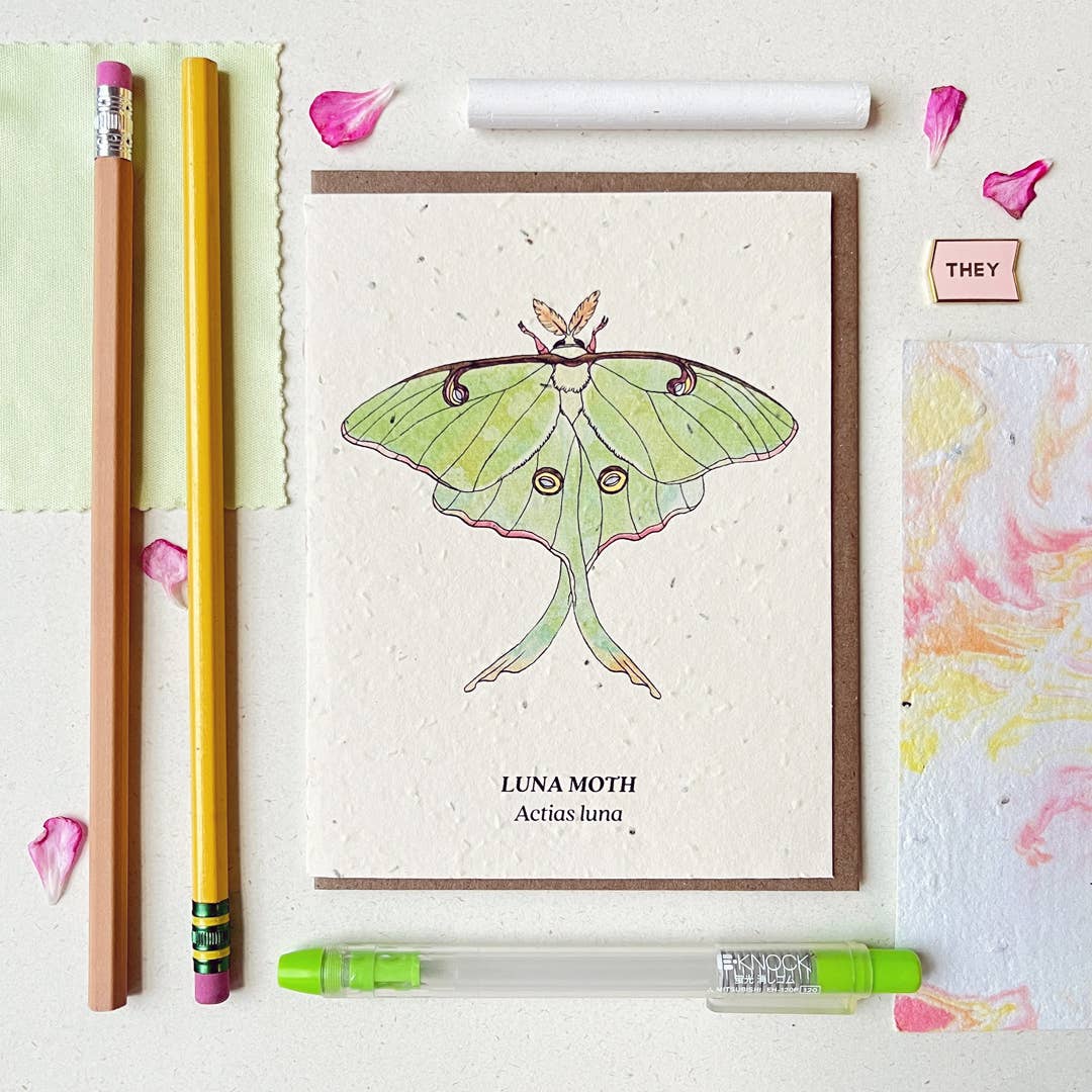 a plantable card depicting a green luna moth surrounded by green office supplies