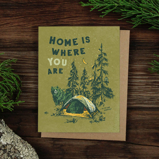 Greeting card with "Home is where you are," featuring a bear and owl near a tent in the woods.