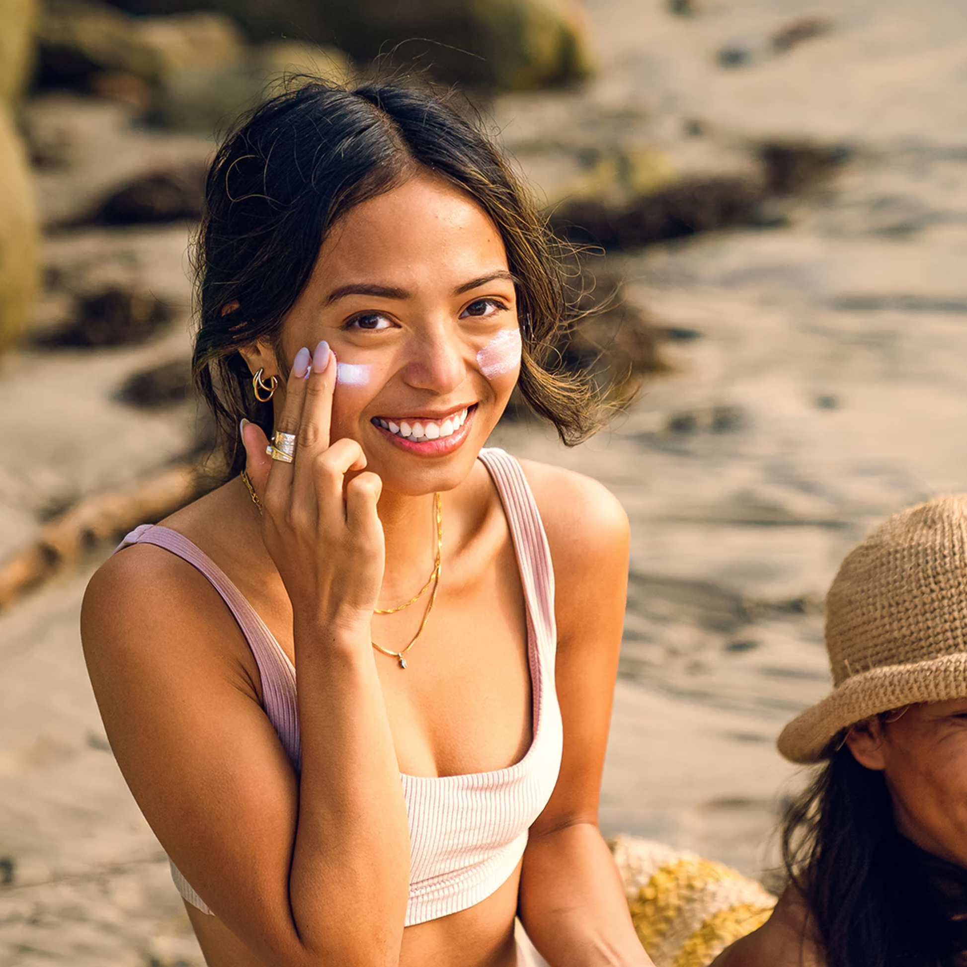 A woman at the beach, smiling and applying Badger Adventure SPF 50 Mineral Sunscreen for sun protection during her outdoor fun.