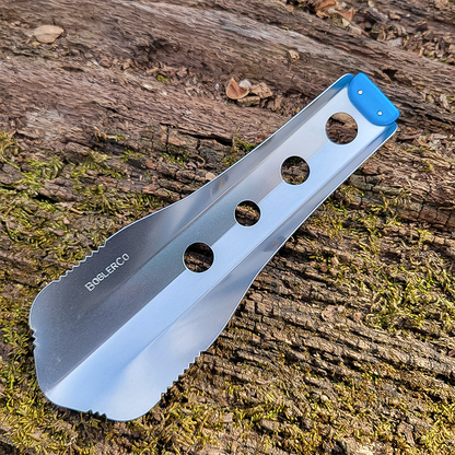 A blue lightweight trowel rests on a tree, showcasing its unique design for ultralight backpacking and outdoor use.