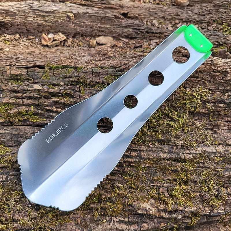 A neon green trowel lies on a tree, highlighting its ergonomic design for backpacking and gardening tasks.