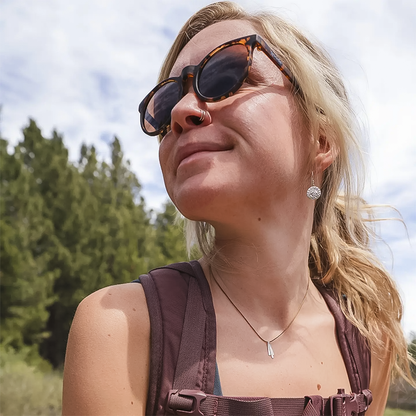 A woman in sunglasses and a backpack, showcasing her adventurous spirit and style with mountain-themed earrings.