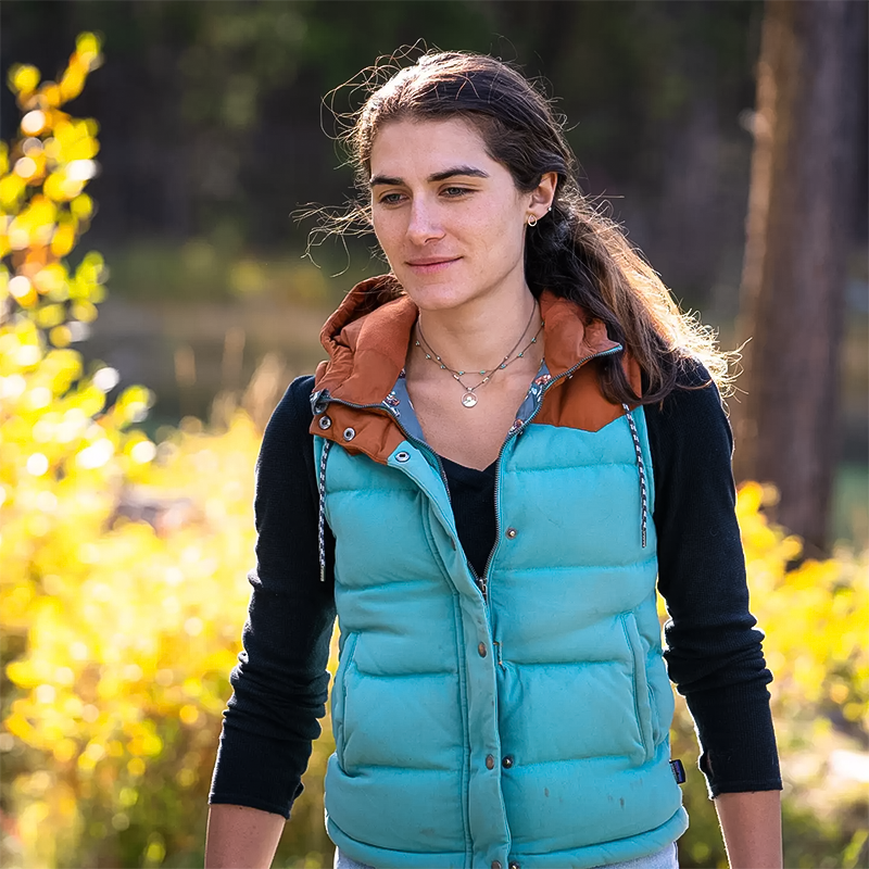 A woman in a turquoise vest wearing a turquoise beaded necklace.