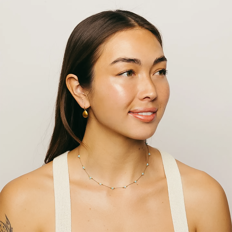 A woman in a white tank top shows a turquoise beaded necklace.