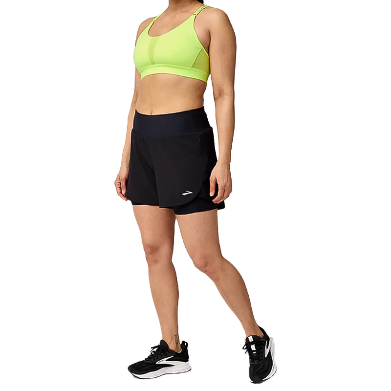 A woman in a black shorts and neon green sports bra, ready for a workout.