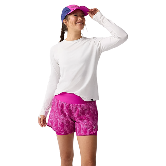 A woman in white Brooks long sleeves and pink running shorts, prepared for a stylish workout.  