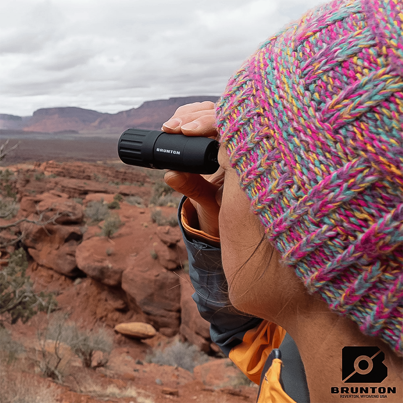 A woman in a pink beanie uses black binoculars to observe nature.  