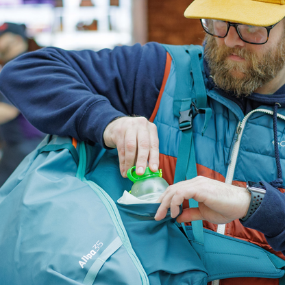 A man in a blue jacket holds a green CNOC 42mm Vesica Collapsible Bottle, showcasing its lightweight and packable design.