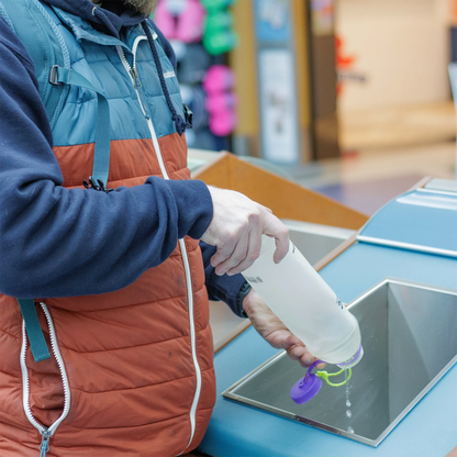 A man pouring water from a purple CNOC 42mm Vesica Collapsible Bottle, showcasing its flexible design and 1L capacity.