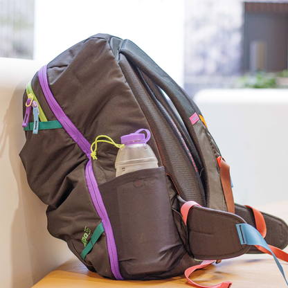 A close-up of a backpack with a purple CNOC 42mm Vesica Collapsible Bottle in its holder, highlighting its convenience for outdoor activities.