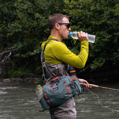 A man stands in water, holding a fishing rod, showcasing the CNOC BiteValve for convenient hydration while fishing.