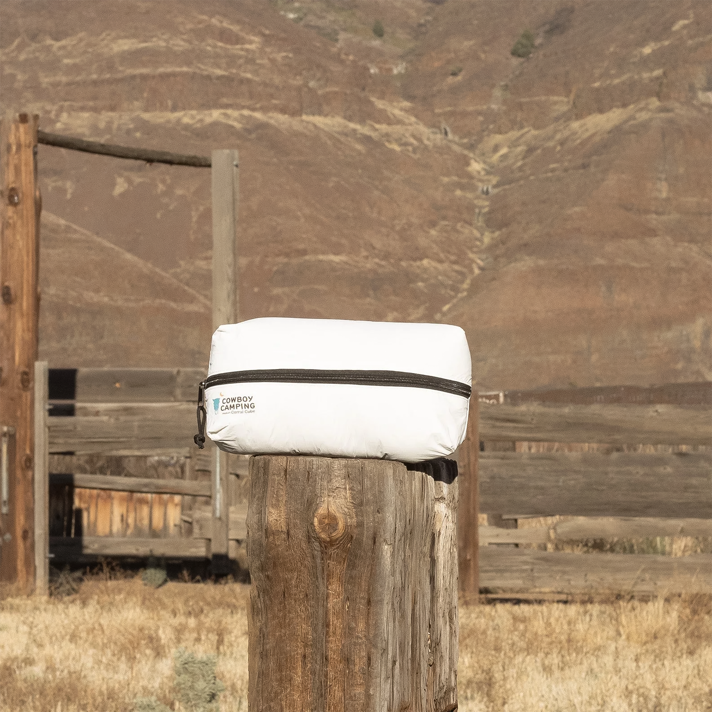 A white camp organizer bag rests on a wooden post in a grassy field, showcasing its compact and durable design.
