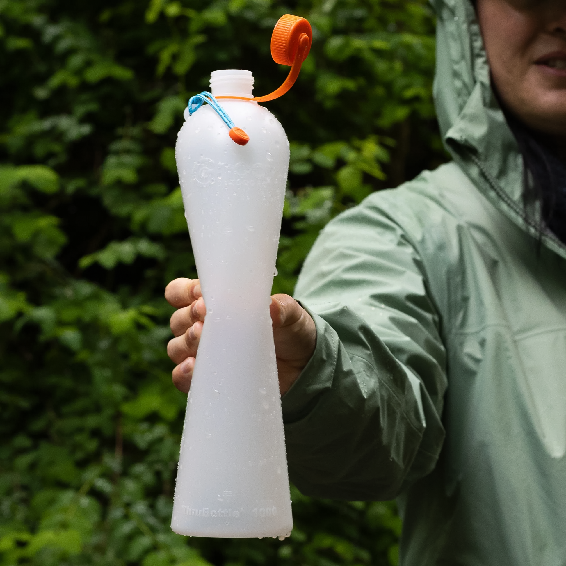 A girl in a rain jacket holds a large white water bottle, showcasing its slim design for ultralight backpacking and hydration.