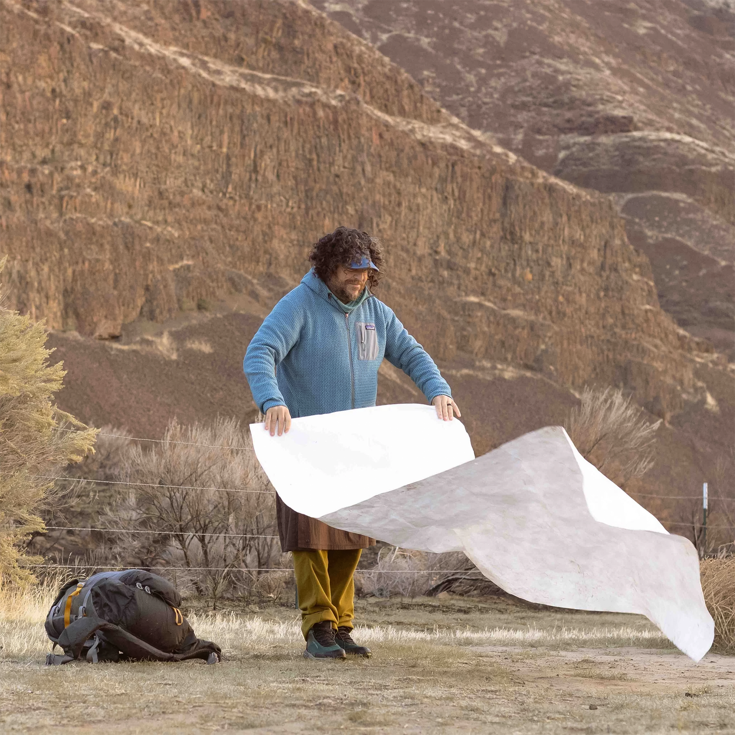 A man holds a large white groundsheet, showcasing its lightweight design for camping and protection from the ground.