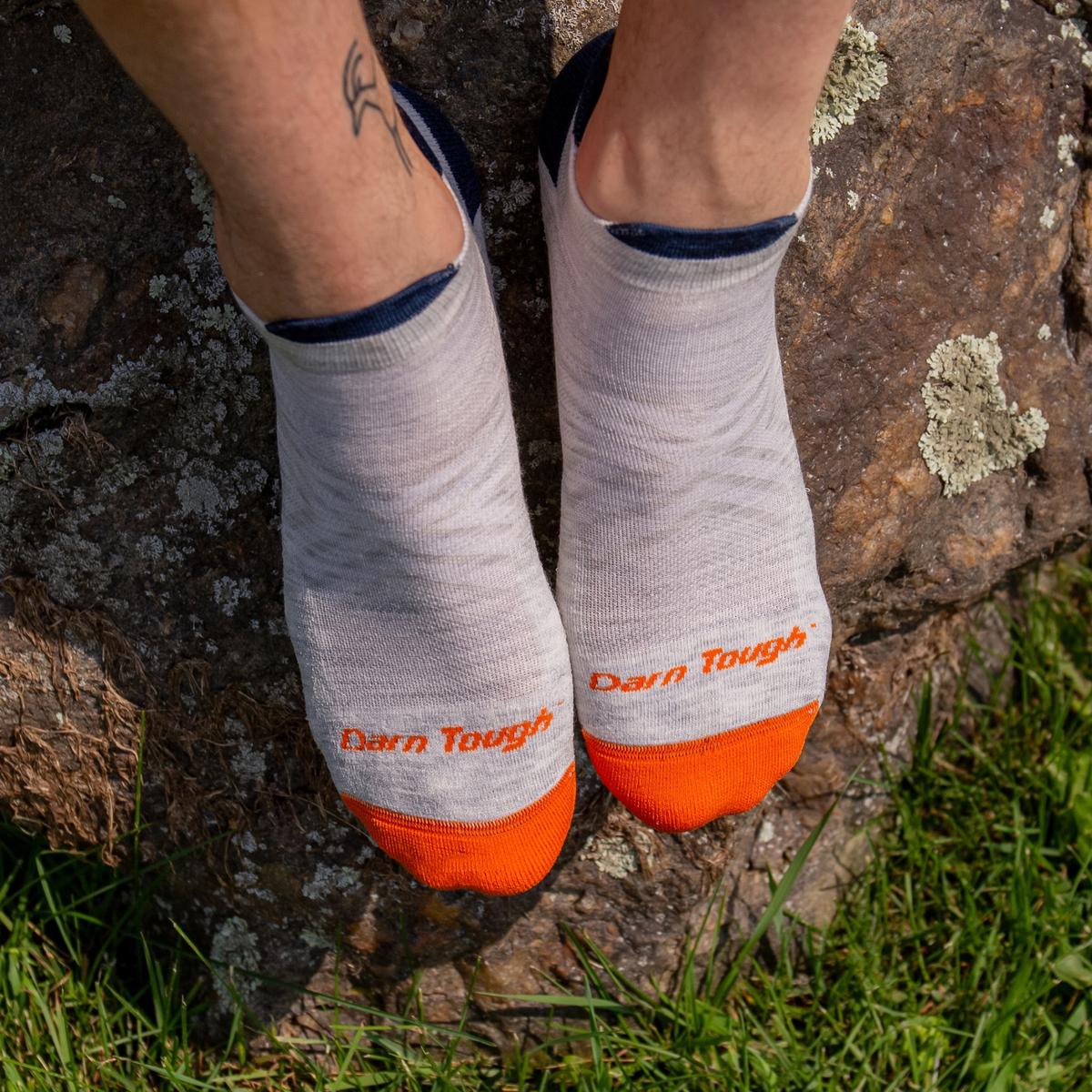 A feet wearing a pair of gray, navy blue, and orange Darn Tough no show running socks.