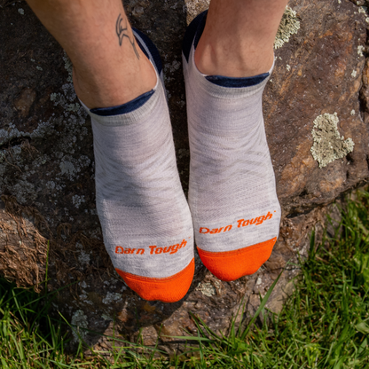 A feet wearing a pair of gray, navy blue, and orange Darn Tough no show running socks.