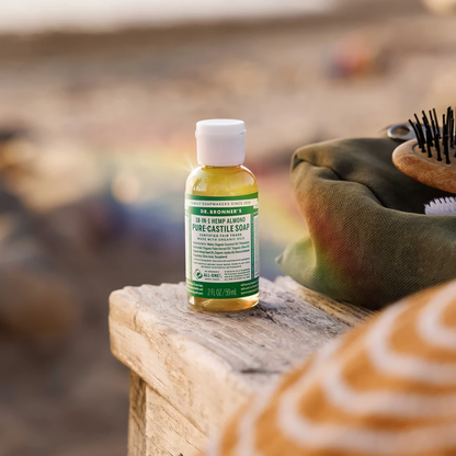 Dr. Bronner's almond Pure-Castile Soap and a brush on a wooden bench, showcasing eco-friendly cleaning products.