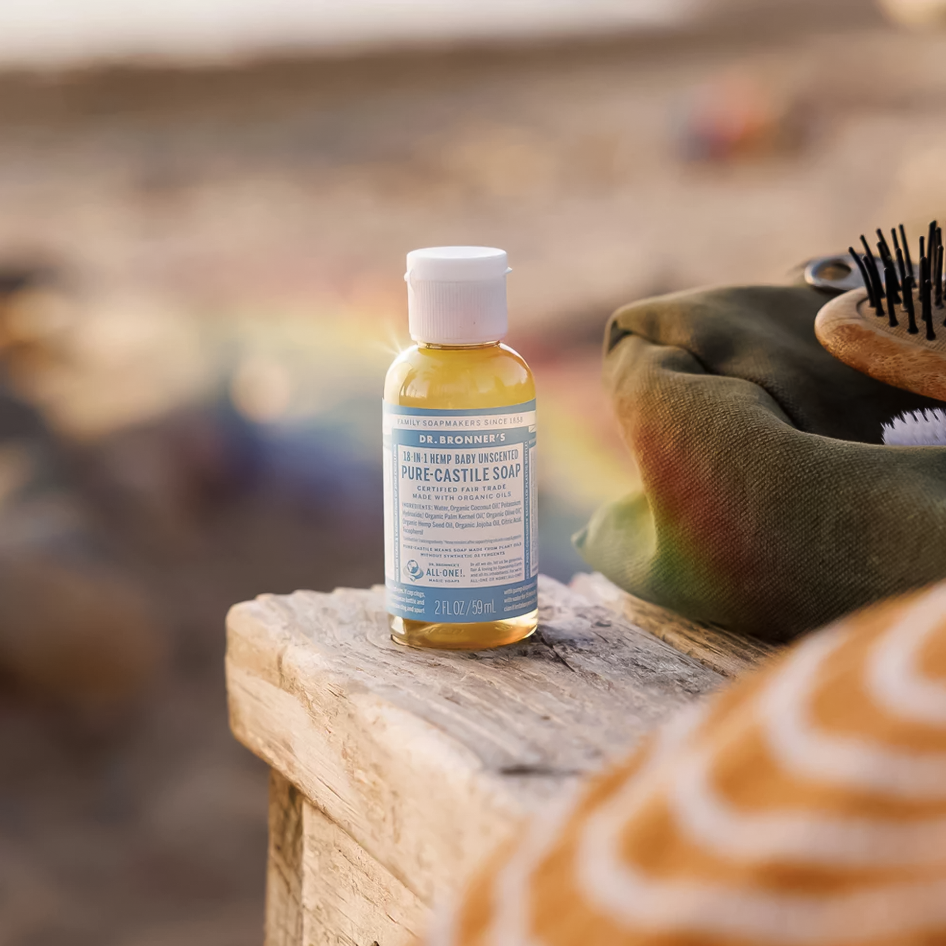 A bottle of Dr. Bronner’s Unscented Pure-Castile Liquid Soap on a bench beside a green pouch.