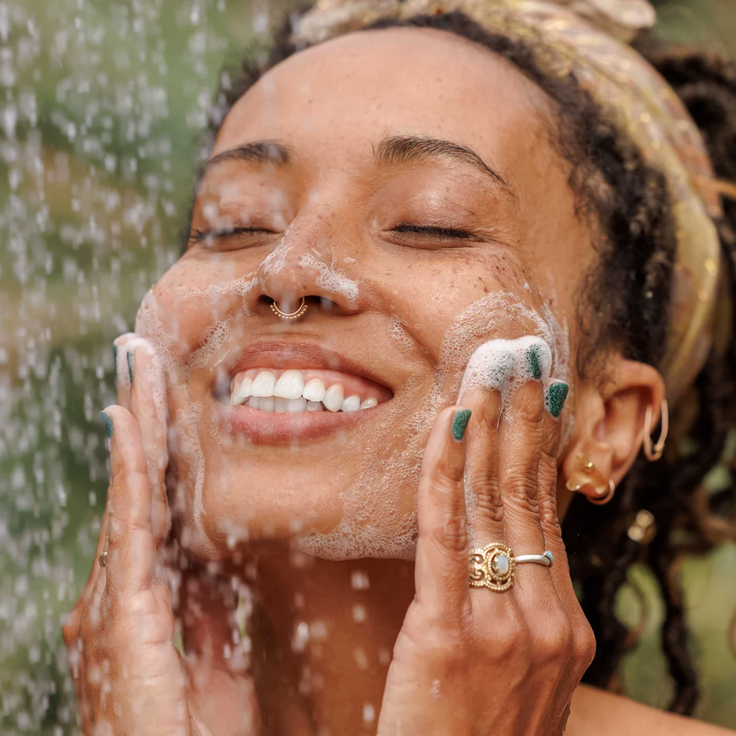 A smiling woman washes her face with Dr. Bronner’s Peppermint Liquid Soap, showcasing its refreshing and uplifting qualities.