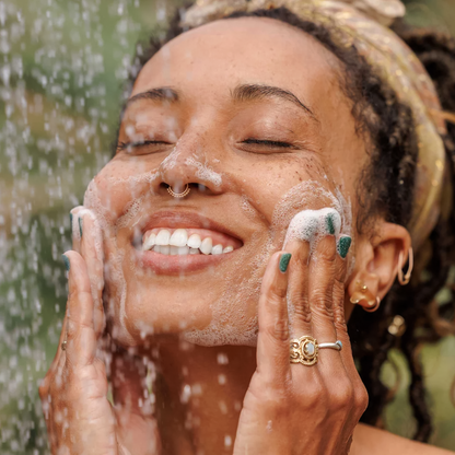 A smiling woman washes her face with Dr. Bronner’s Peppermint Liquid Soap, showcasing its refreshing and uplifting qualities.