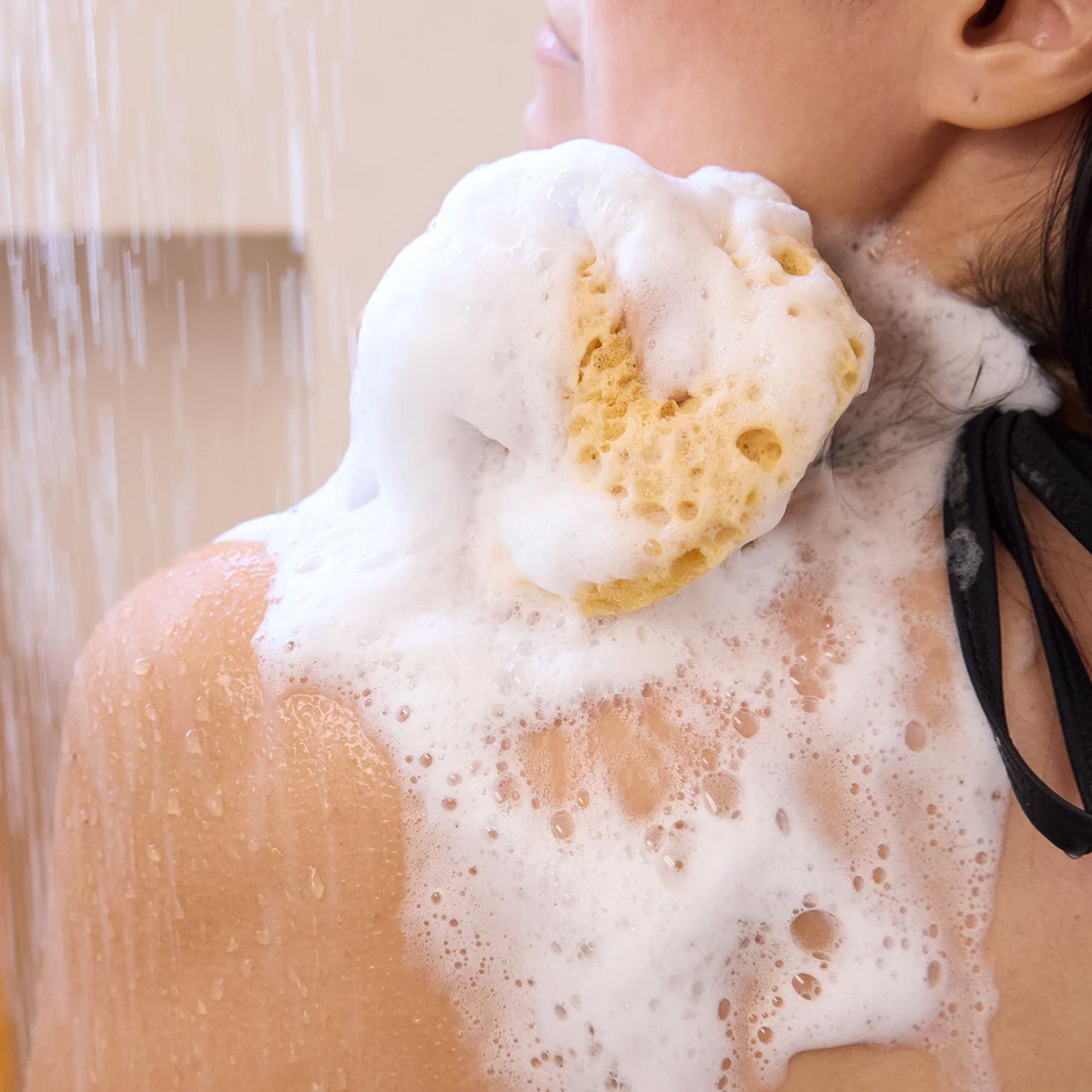 A woman lathers her back with Dr. Bronner’s Peppermint Liquid Soap in a bright bathroom setting.