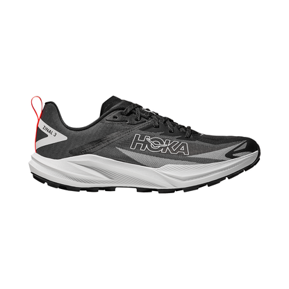 Black and white Hoka Zinal 3 trail running shoes on a rocky path, showcasing their lightweight design and aggressive lugs for traction.