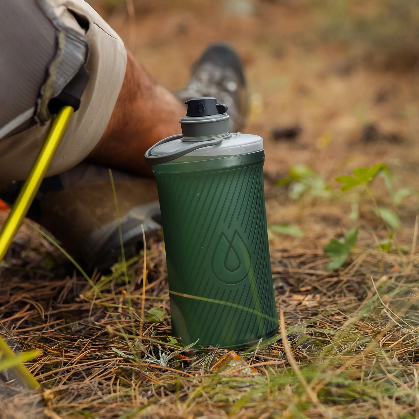 Green compact Hydrapak collapsible water bottle placed on the ground designed with hard bottle stability combined with soft flask convenience, ideal for hydration on-the-go.