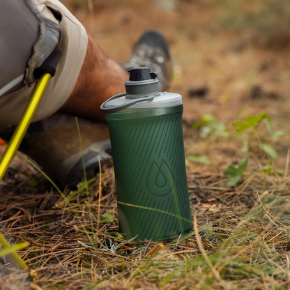 Green compact Hydrapak collapsible water bottle placed on the ground designed with hard bottle stability combined with soft flask convenience, ideal for hydration on-the-go.