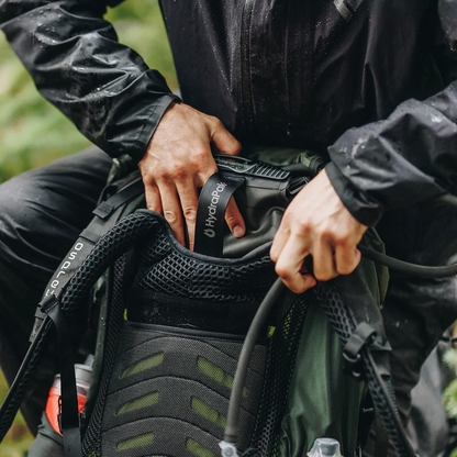 A man in a rain jacket putting the HydraPak Force DSL hydration reservoir inside his backpack.