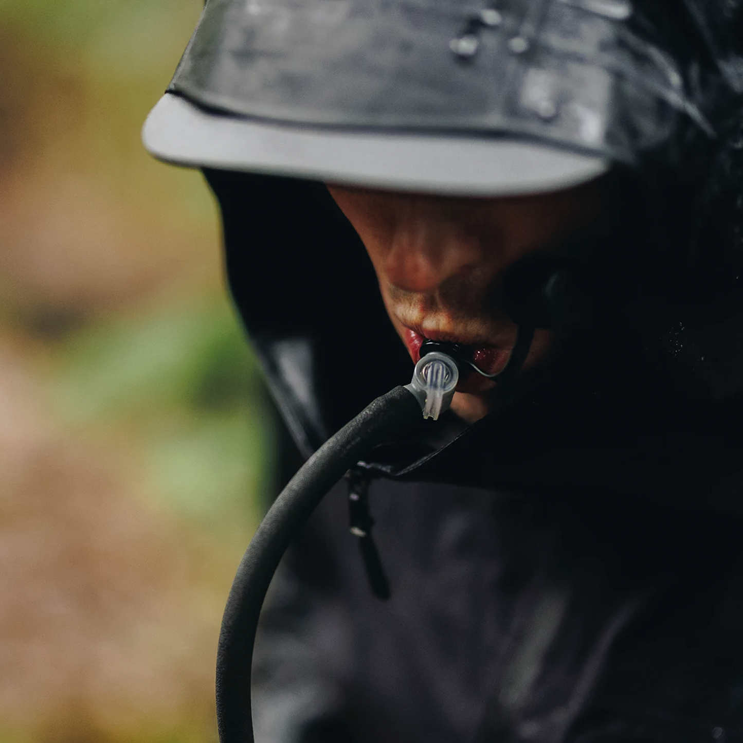 A man in a rain jacket and helmet holds a HydraPak Force DSL hydration reservoir, showcasing its rugged design and features.