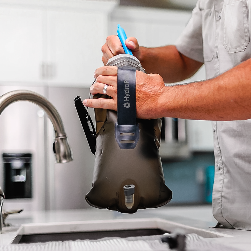 A man uses brush to clean his Hydrapak water bottle in his sink.