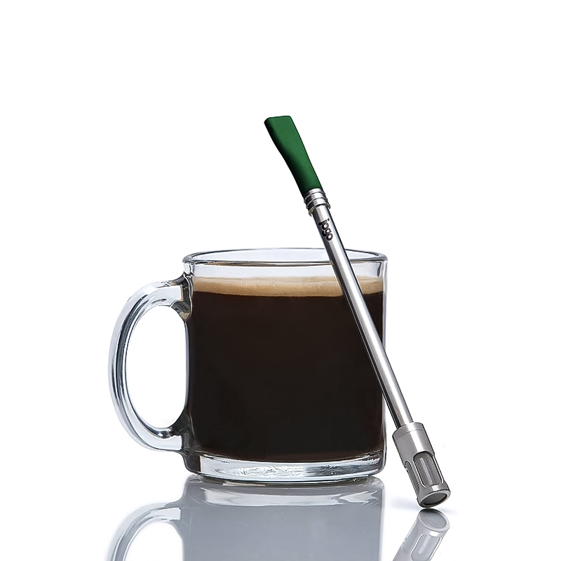 A cup of coffee with a green portable brewing straw for coffee and tea on the side.