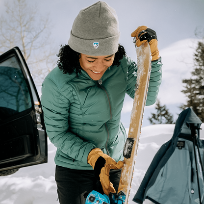 Person in winter gear wearing a kuhl merino beanie preparing skis in a snowy outdoor setting