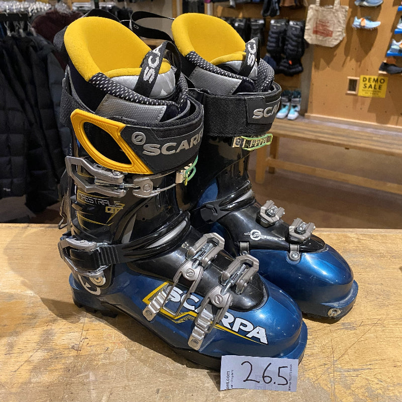 Pair of blue and black ski boots with yellow accents on a wooden surface.