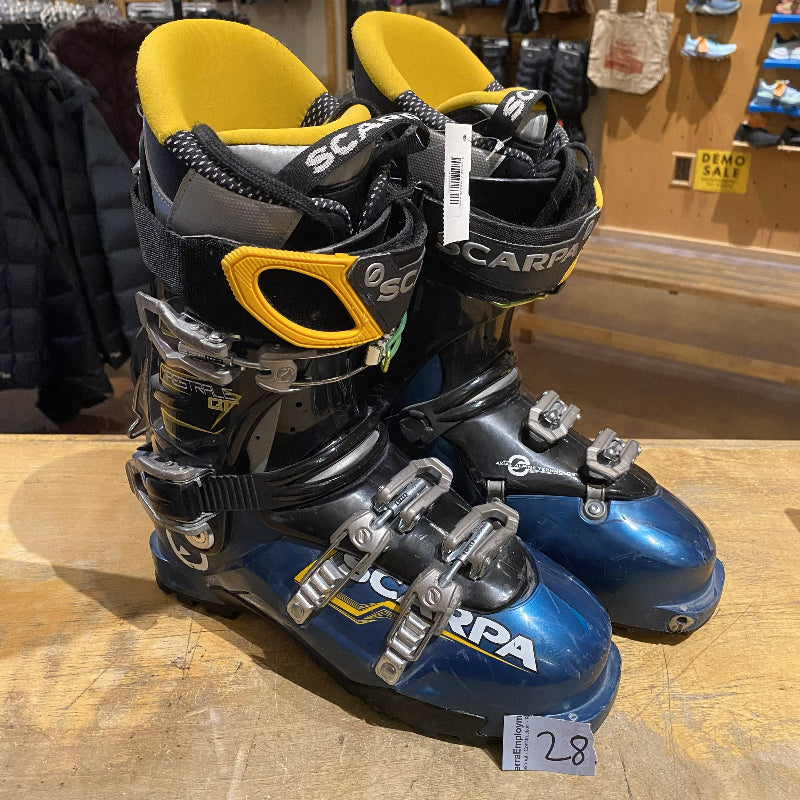 Pair of blue and black ski boots with yellow accents on a wooden surface, brand 'Scarpa' visible
