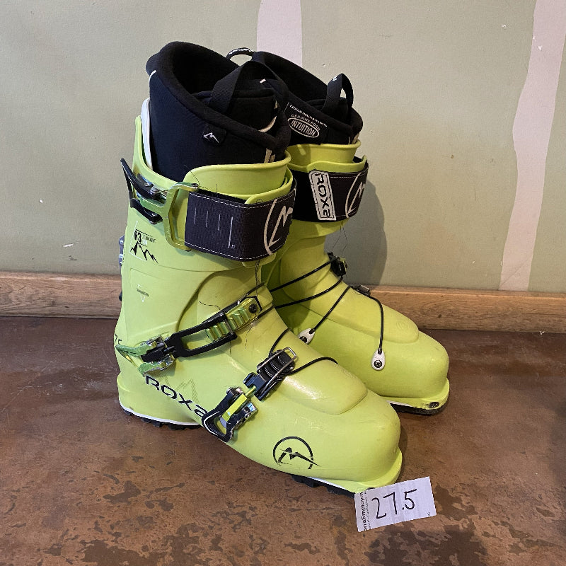 Pair of neon green ski boots with black accents on a brown surface.
