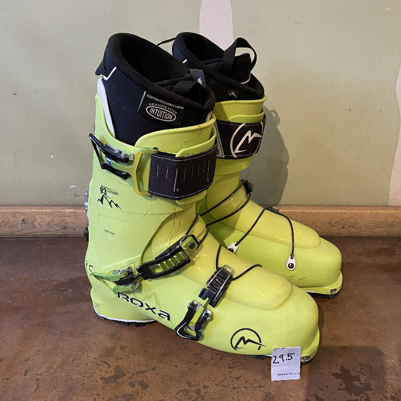 Pair of yellow ski boots with black accents on a wooden floor.