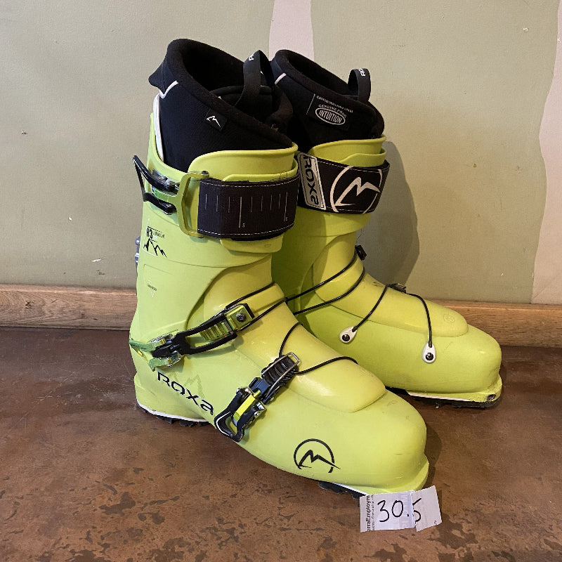 Pair of yellow ski boots with black straps on a wooden floor.